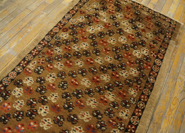 A tan rug with dense stylized patterns in black, red, and cream on distressed wood floors.