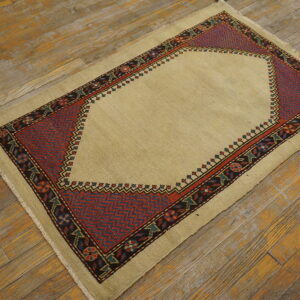 Low-pile beige rug featuring a dark red and blue geometric mihrab design on aged wood floors.