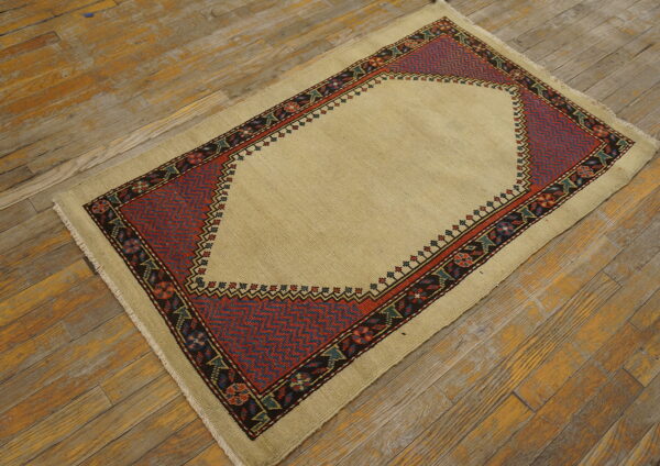 Low-pile beige rug featuring a dark red and blue geometric mihrab design on aged wood floors.