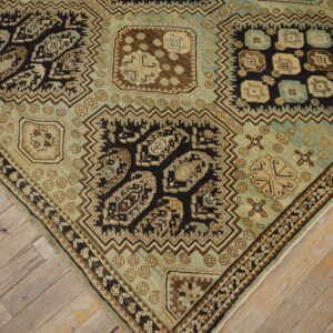 Ornate rug corner featuring geometric motifs in teal, dark brown, and beige over weathered wood floors.