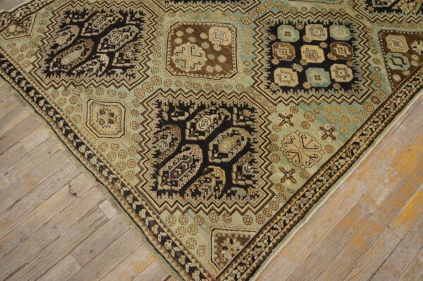 Ornate rug corner featuring geometric motifs in teal, dark brown, and beige over weathered wood floors.