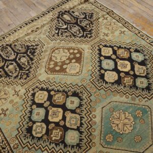 Geometric panel rug in shades of teal, black, tan, and brown rests on distressed light wooden flooring.