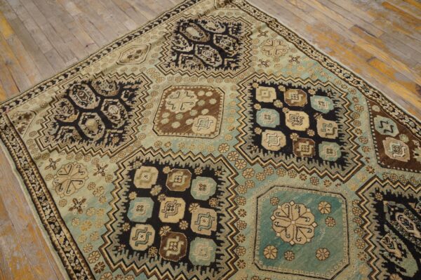 Geometric panel rug in shades of teal, black, tan, and brown rests on distressed light wooden flooring.