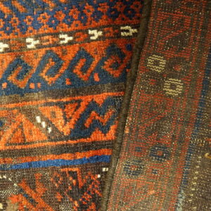Closeup of a folded rug displays orange and blue pile patterns contrasting with the dark brown reverse side.