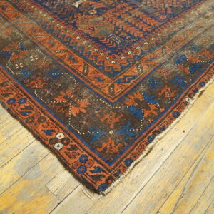 Dark geometric rug corner in blue and rust sits on worn, wide-plank wood flooring.