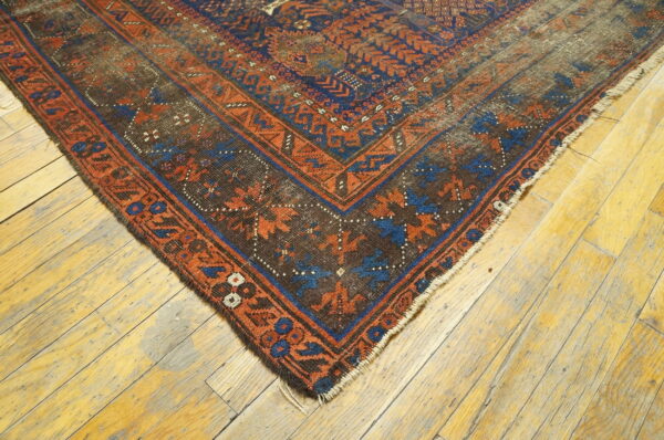 Dark geometric rug corner in blue and rust sits on worn, wide-plank wood flooring.