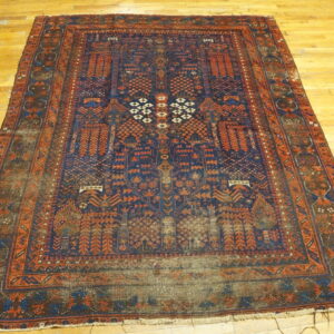 Worn traditional low-pile rug featuring complex navy and rust geometric patterns on a light wood floor.