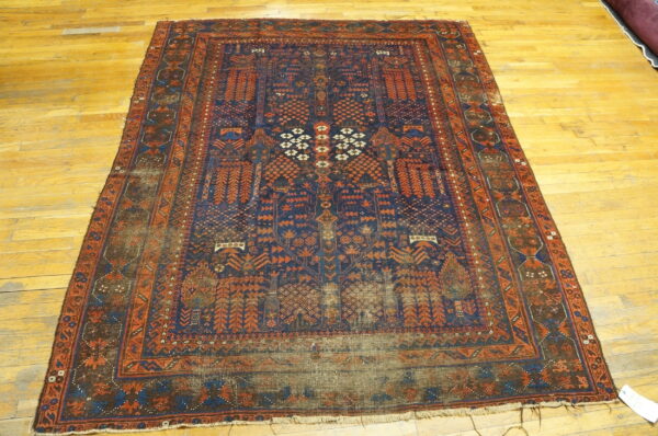 Worn traditional low-pile rug featuring complex navy and rust geometric patterns on a light wood floor.