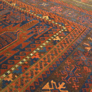 Geometric patterned rug detail showing colors of terracotta red, deep indigo, and dark brown.