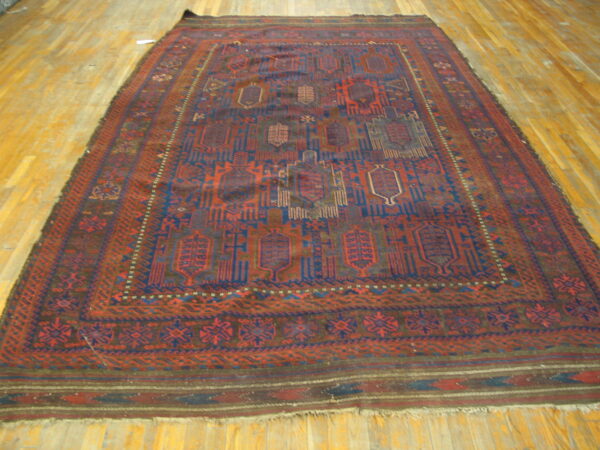 Low-pile red and navy rug with repeating geometric medallions and multiple borders on a wood floor.