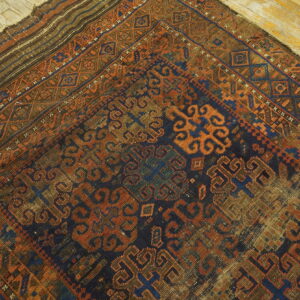 Geometric patterned rug in rich indigo, orange, and brown lies diagonally on weathered wood planks.
