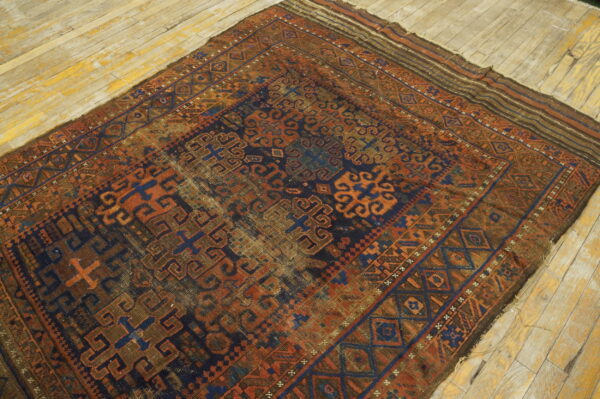 Distressed, low-pile rug featuring complex geometric patterns in navy blue, rust, and brown on a rustic wood floor.