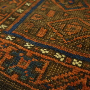Detailed close-up of a geometric rug showing rust, dark blue, brown, and cream pile texture.
