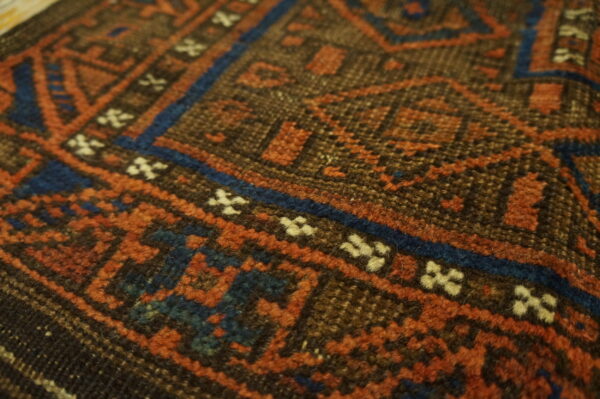 Detailed close-up of a geometric rug showing rust, dark blue, brown, and cream pile texture.