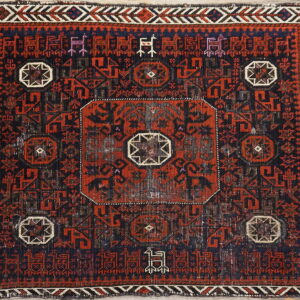 Geometric red and dark blue rug with stylized figures and medallions placed on light wood floors.