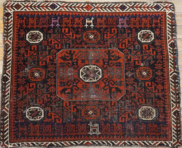 Geometric red and dark blue rug with stylized figures and medallions placed on light wood floors.