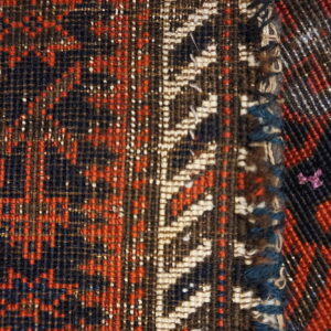 Low-pile rug section in red and navy meets a contrasting diagonal woven border.