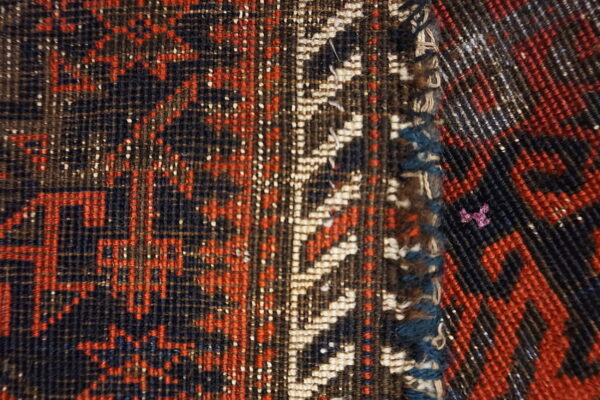 Low-pile rug section in red and navy meets a contrasting diagonal woven border.