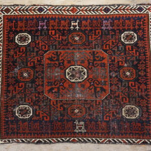 Dark red and navy geometric rug with center medallion and stylized border figures on light wooden floors.