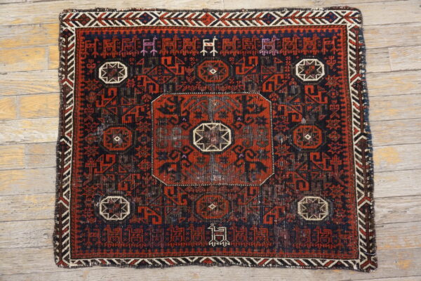 Dark red and navy geometric rug with center medallion and stylized border figures on light wooden floors.