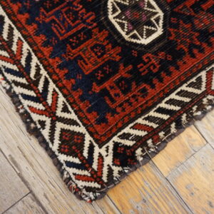 Geometric rug in red, cream, and dark blue on rustic, gray-washed wood flooring.