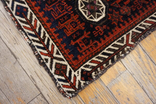 Geometric rug in red, cream, and dark blue on rustic, gray-washed wood flooring.