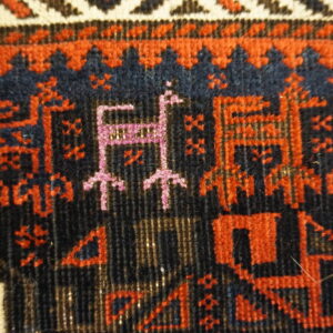 Low pile rug detail showing deep navy field with reddish-orange and magenta geometric figures.