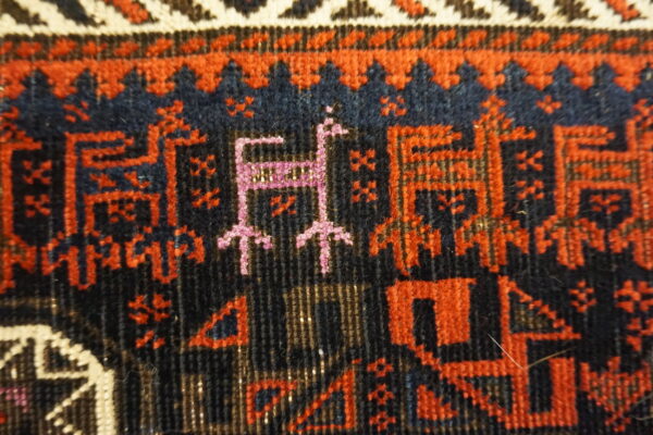 Low pile rug detail showing deep navy field with reddish-orange and magenta geometric figures.