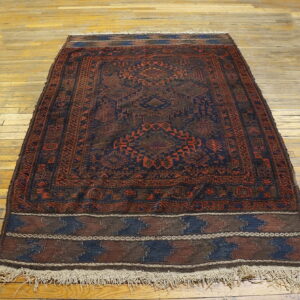 Geometric dark blue and red patterned rug with fringes lies on light plank wood floor.