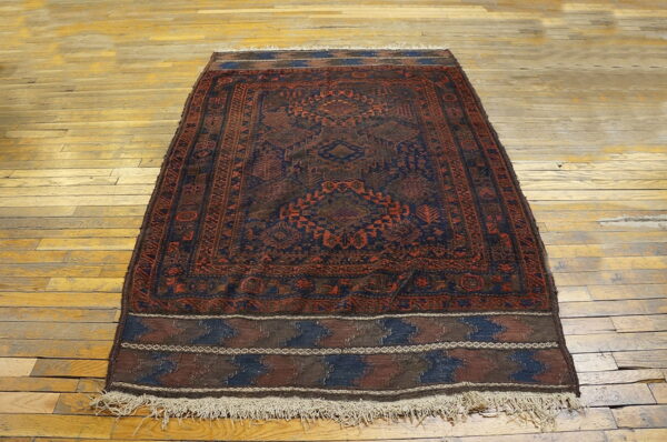 Geometric dark blue and red patterned rug with fringes lies on light plank wood floor.