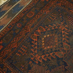 Dark blue and rust geometric rug layered over a striped rug on weathered wood flooring.