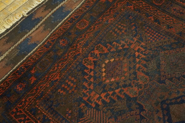 Dark blue and rust geometric rug layered over a striped rug on weathered wood flooring.