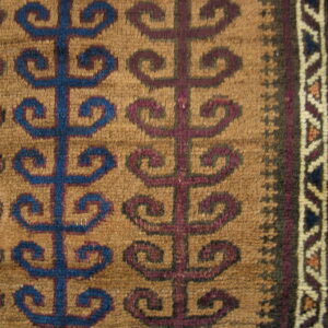 Detailed close-up of a woven rug featuring blue and maroon repeating scroll motifs on a light brown background.