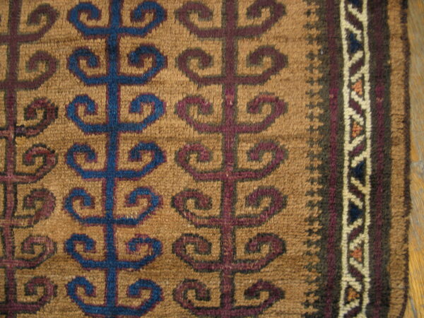 Detailed close-up of a woven rug featuring blue and maroon repeating scroll motifs on a light brown background.