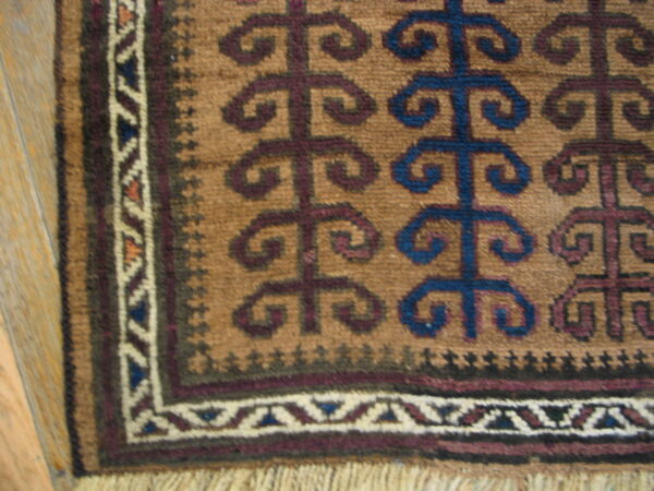 Brown and tan rug detail with repeating blue and purple scrolling motifs, a geometric border, and light fringe.