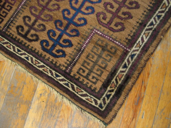 Brown low-pile rug with geometric blue and purple traditional motifs on light distressed hardwood.