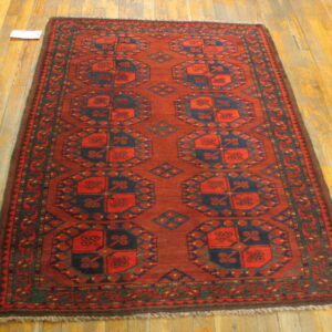 Rust-colored geometric runner rug with navy motifs and fringed edges on wooden flooring.