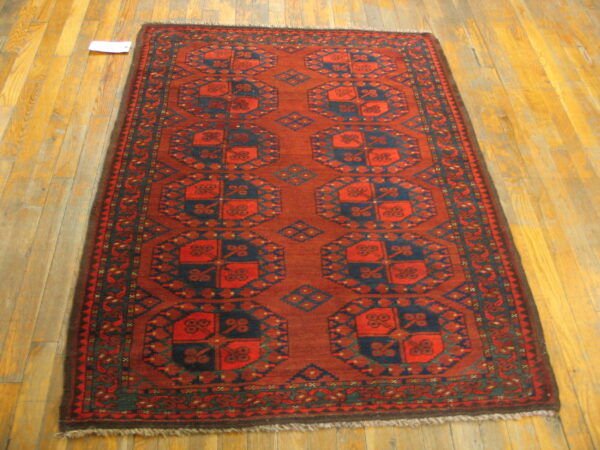 Rust-colored geometric runner rug with navy motifs and fringed edges on wooden flooring.