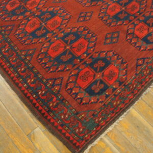 Deep red and navy geometric rug with repeating medallion patterns rests on light wood planks.