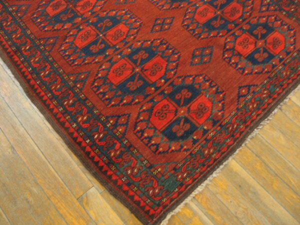 Deep red and navy geometric rug with repeating medallion patterns rests on light wood planks.