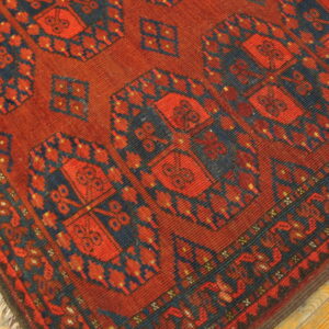 This rug features dense red and blue traditional geometric patterns on light wooden floorboards.