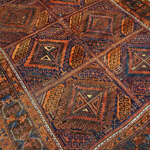 Low-pile rug with intricate geometric squares in indigo, rust, and brown rests on light wood planks.