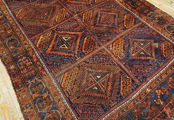 Low-pile rug with intricate geometric squares in indigo, rust, and brown rests on light wood planks.