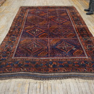 Traditional geometric rug in deep blues and warm oranges displayed on a worn wood floor.