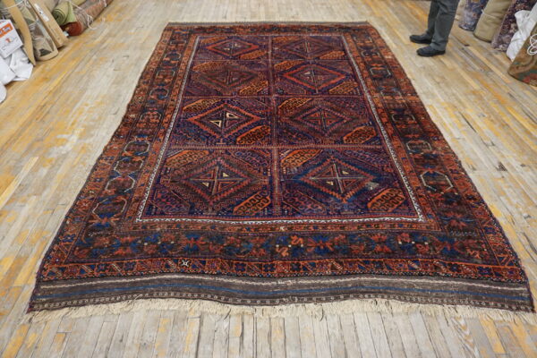 Traditional geometric rug in deep blues and warm oranges displayed on a worn wood floor.