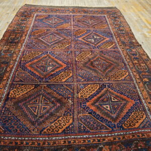 A richly patterned rug featuring repeating blue and rust geometric diamond panels on light wood.