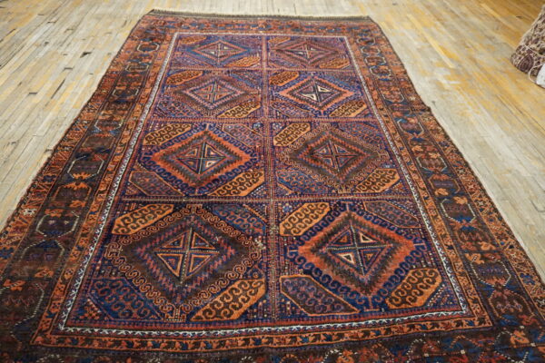 A richly patterned rug featuring repeating blue and rust geometric diamond panels on light wood.