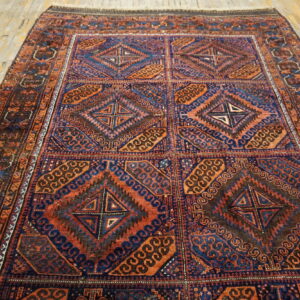 A tribal-style rug featuring deep blue, orange, and brown geometric patterns is laid on rustic wood planks.