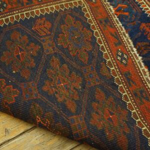 Detail of a dark geometric rug with red and blue patterns, folded on weathered wood flooring.
