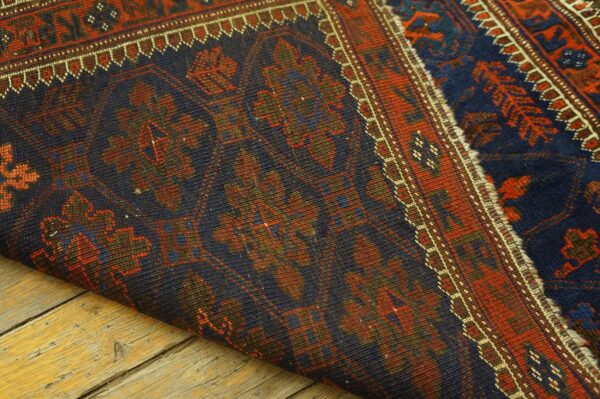 Detail of a dark geometric rug with red and blue patterns, folded on weathered wood flooring.